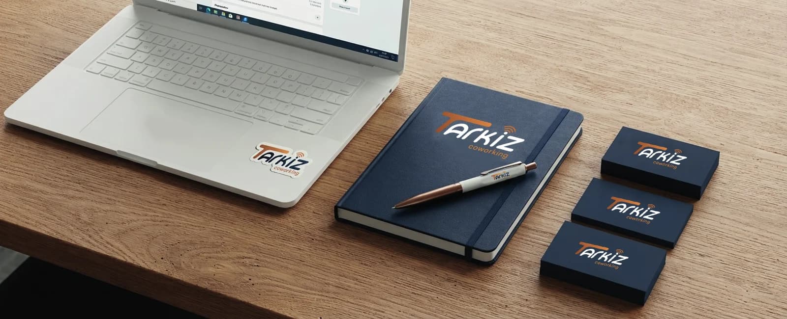 Un ordinateur, un carnet et de la papeterie Tarkiz sur un bureau en bois